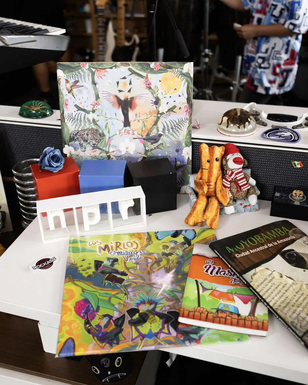 Vinilo de The World Meets Los Mirlos, libros sobre Moyobamba y el logo de NPR sobre el escritorio de Tiny Desk