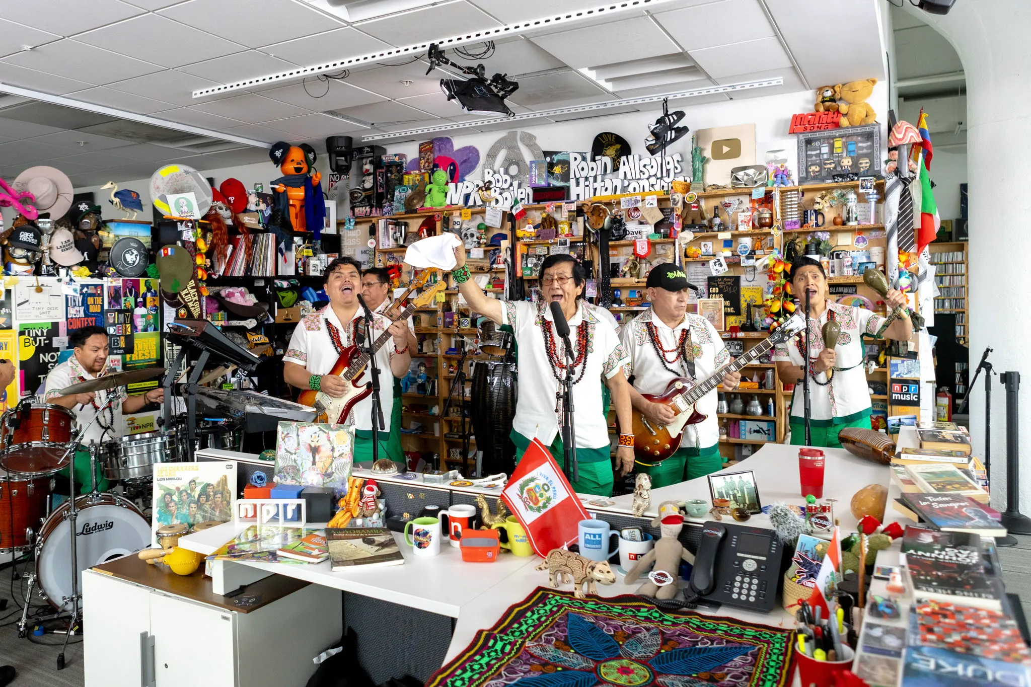 Los Mirlos tocando en NPR Tiny Desk con camisas bordadas con arte kené y una bandera del Perú sobre el escritorio